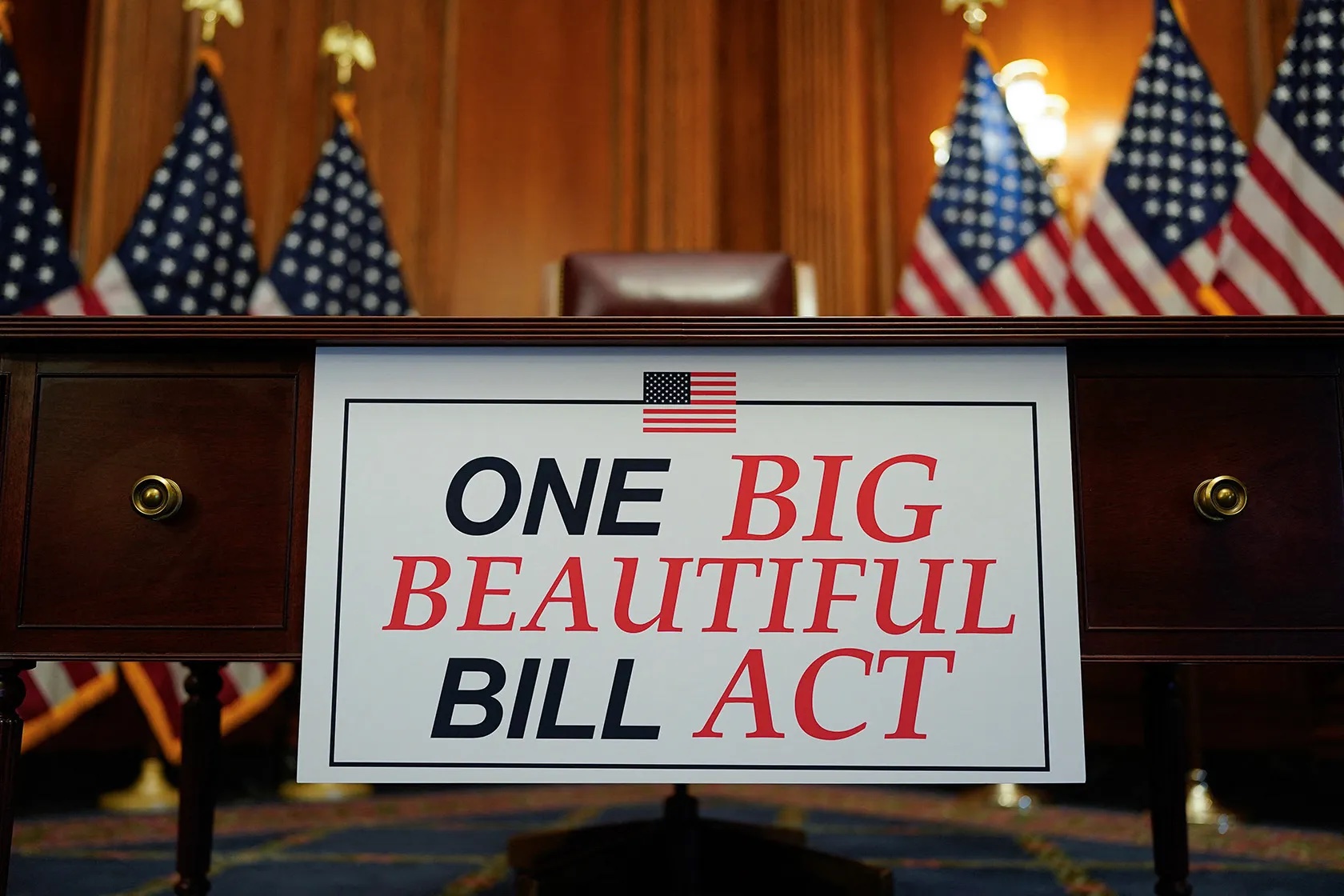 Congressional podium with 'ONE BIG BEAUTIFUL BILL ACT' sign surrounded by American flags in formal government chamber
